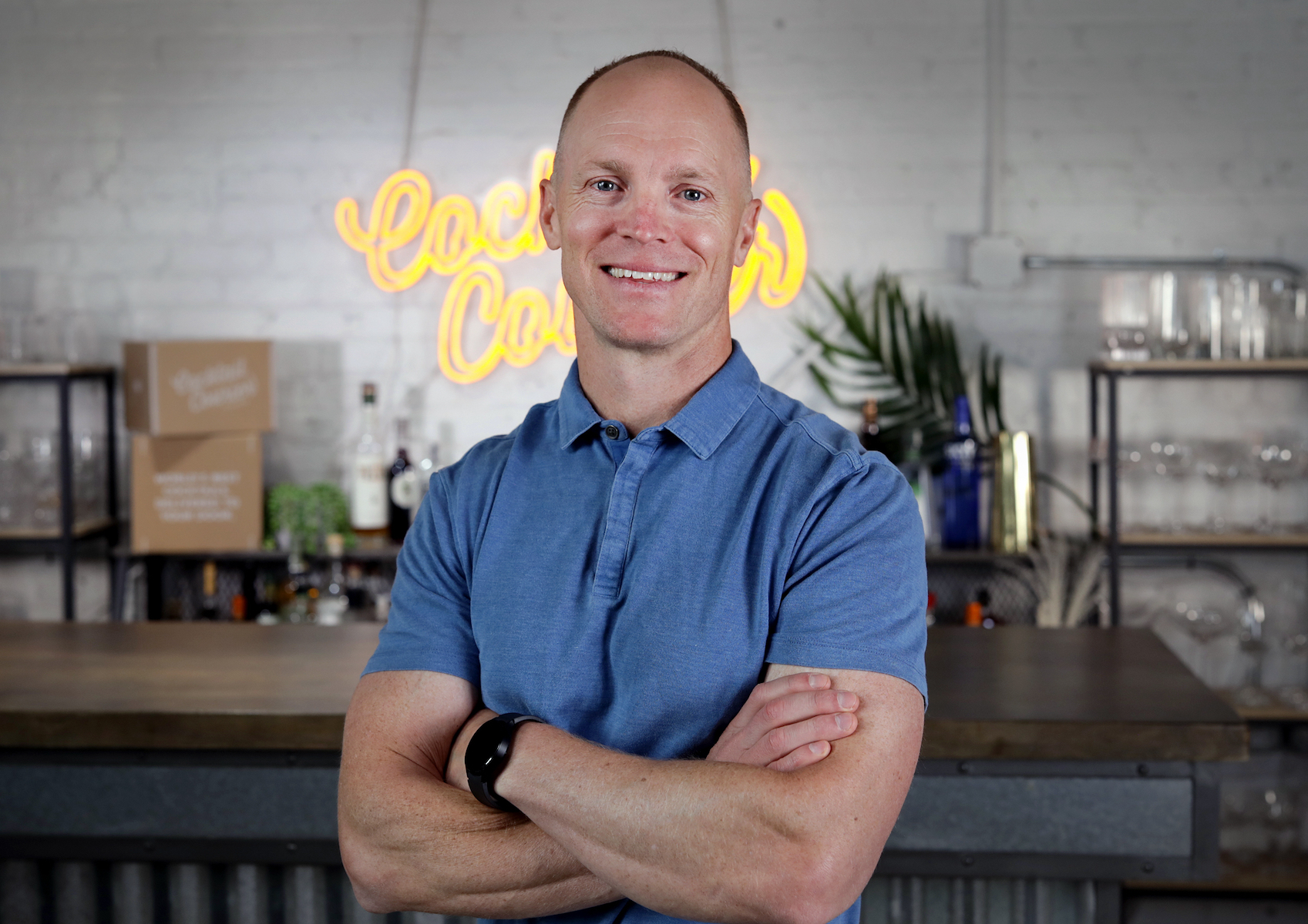 Scott Goldman CEO and Founder of Cocktail Courier posing with arms crossed in front of neon Cocktail Courier sign